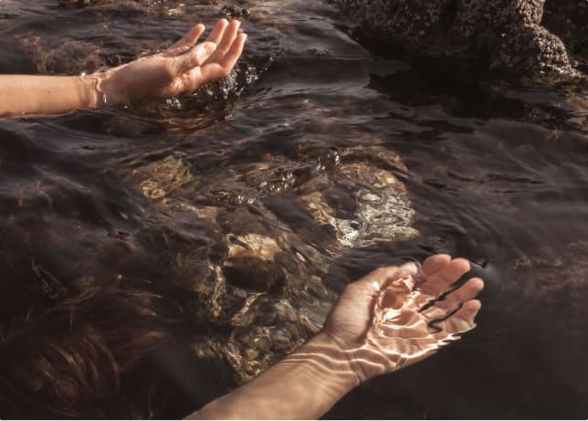 Hands cupping dark rock-pool water.